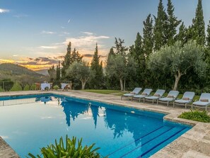 Une piscine entourée d’arbres, avec des chaises longues et des tables, et offrant une vue sur les collines.