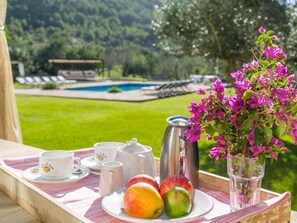 A breakfast setup with a tray, fruits, a coffee pot, cups, and a vase of flowers. - Historic Finca in Mallorca with Pool for 12 Guests (Andratx)