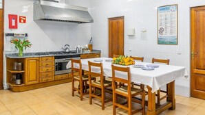 A kitchen with a dining table set for four, wooden cabinets, a stainless steel range hood, and a calendar on the wall.