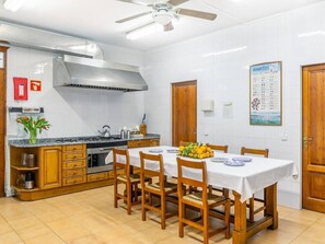 A kitchen with a dining table set for four, wooden cabinets, a stainless steel range hood, and a calendar on the wall.
