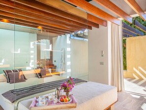 A modern bedroom with a glass wall, a bed with a tray of breakfast, and a view of a bathroom and outdoor area. - Historic Finca in Mallorca with Pool for 12 Guests (Andratx)