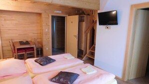 Una habitación tipo cabaña de madera con dos camas, un televisor y una escalera.