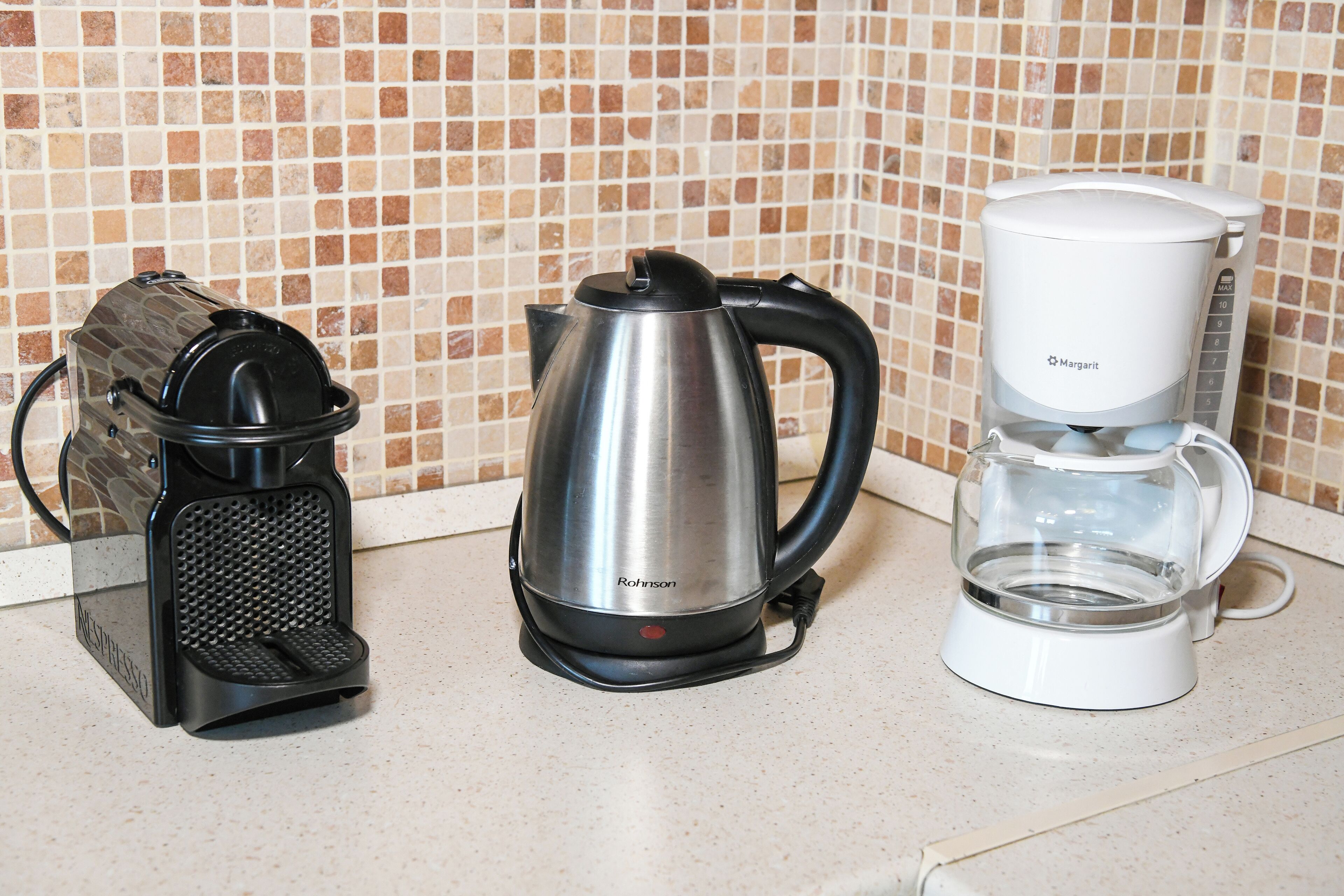 A kitchen counter with a coffee maker, a kettle, and a coffee pot.