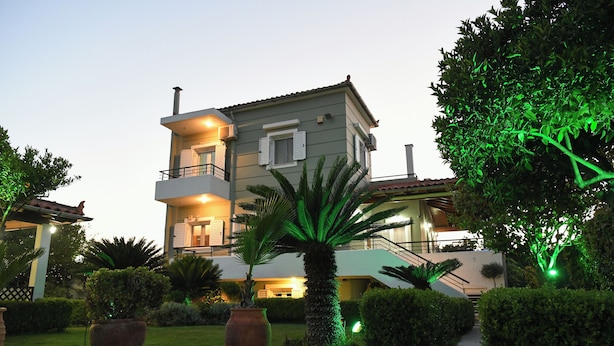 A multi-story building with a balcony, surrounded by well-maintained hedges and palm trees, with green lighting accents.
