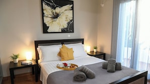 A neatly made bed with a tray of breakfast items, a potted plant, and rolled towels on a wooden bed frame in a hotel room.