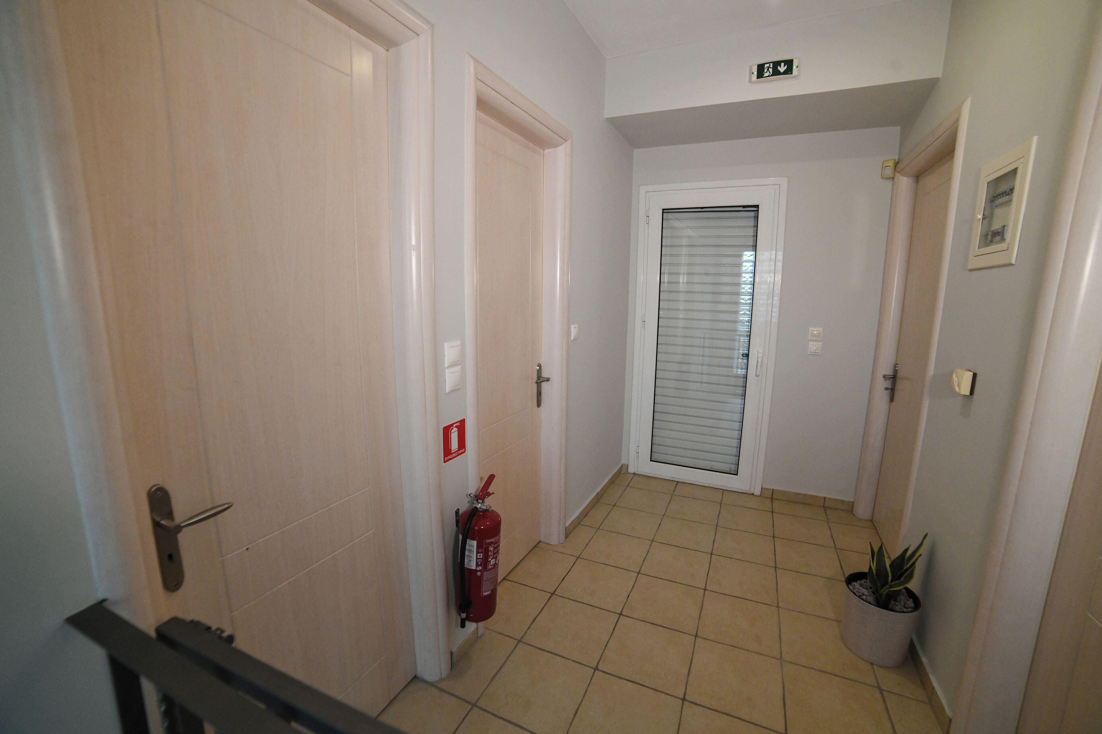 A hallway with a fire extinguisher, a potted plant, and a door with a sign.