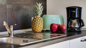 Un comptoir de cuisine avec un évier en acier inoxydable, un grille-pain, une machine à café, un ananas et deux pommes.