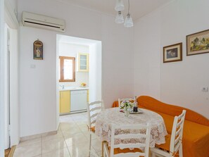 A dining area with a table set for two, a kitchen in the background, and a single window.