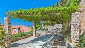 A stone patio with lounge chairs under a pergola, a stone wall, and a view of red-roofed buildings. - Apartments Marija, (12033), Dubrovnik, hr (Dubrovnik)