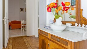 A hallway with a wooden cabinet, a white vase with flowers, and a mirror reflecting a painting. - Apartments Marija, (12033), Dubrovnik, hr (Dubrovnik)