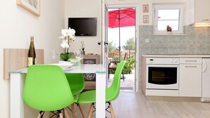 Une cuisine moderne avec des meubles blancs, un four encastré et un coin repas comprenant une table en verre et des chaises vertes.