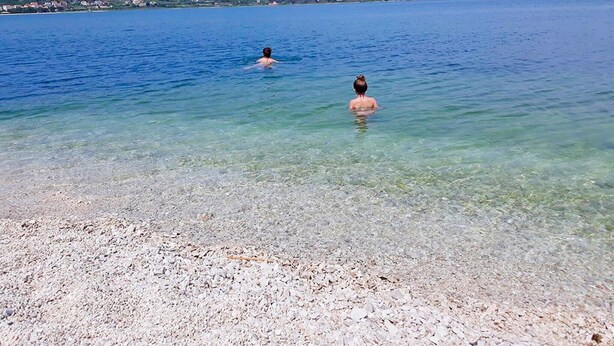 Un lac aux eaux limpides où nagent deux personnes, bordé d’une rive rocheuse et entouré de collines lointaines.