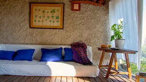 A white sofa with blue cushions, a framed botanical print, a small table with a potted plant, and a rustic wall.