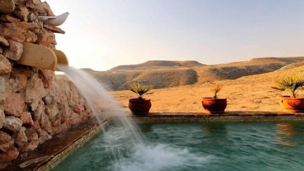 A pool with a waterfall feature, surrounded by potted plants and a desert landscape in the background.
