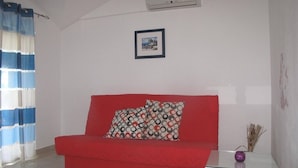 A red sofa with patterned cushions, a framed picture on the wall, and a small table with a vase. - Apartments Antonija, (12172), Stari Grad, hr (Stari Grad)