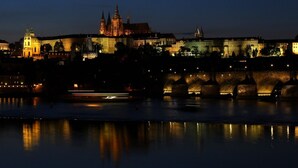 Vista nocturna de un paisaje urbano histórico con edificios iluminados y un puente sobre un río.