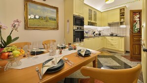 Un comedor con una mesa preparada para cuatro personas, un cuadro en la pared y una cocina al fondo.