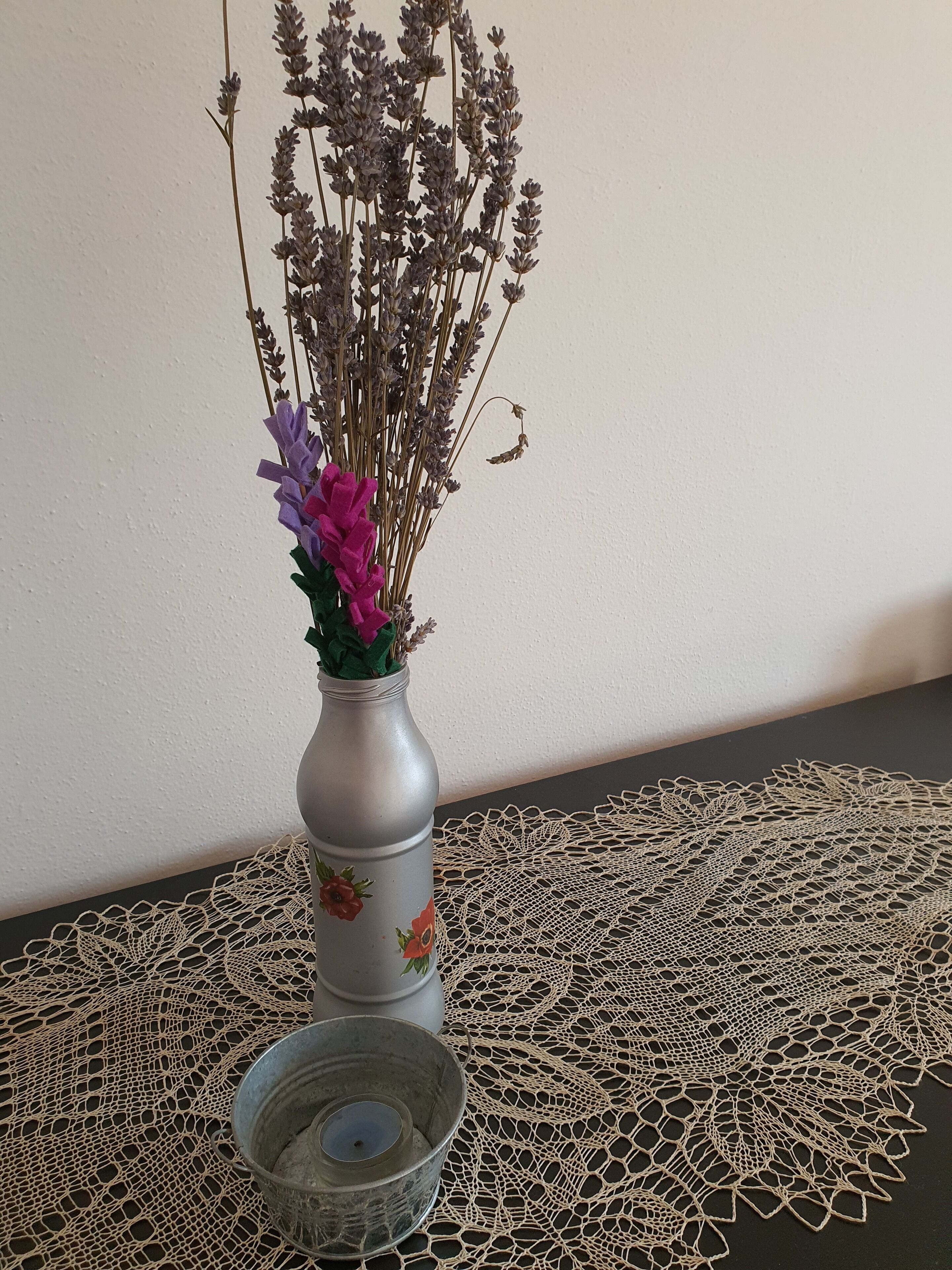 Un jarrón con flores secas y una vela sobre un mantel de encaje.