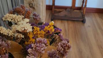 A room with a wooden floor, a spinning wheel, and a bouquet of dried flowers in the foreground.