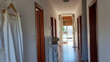 A hallway with wooden flooring, white walls, and doors leading to rooms. There are white garments hanging on a rack and a basket with green plants on a table.