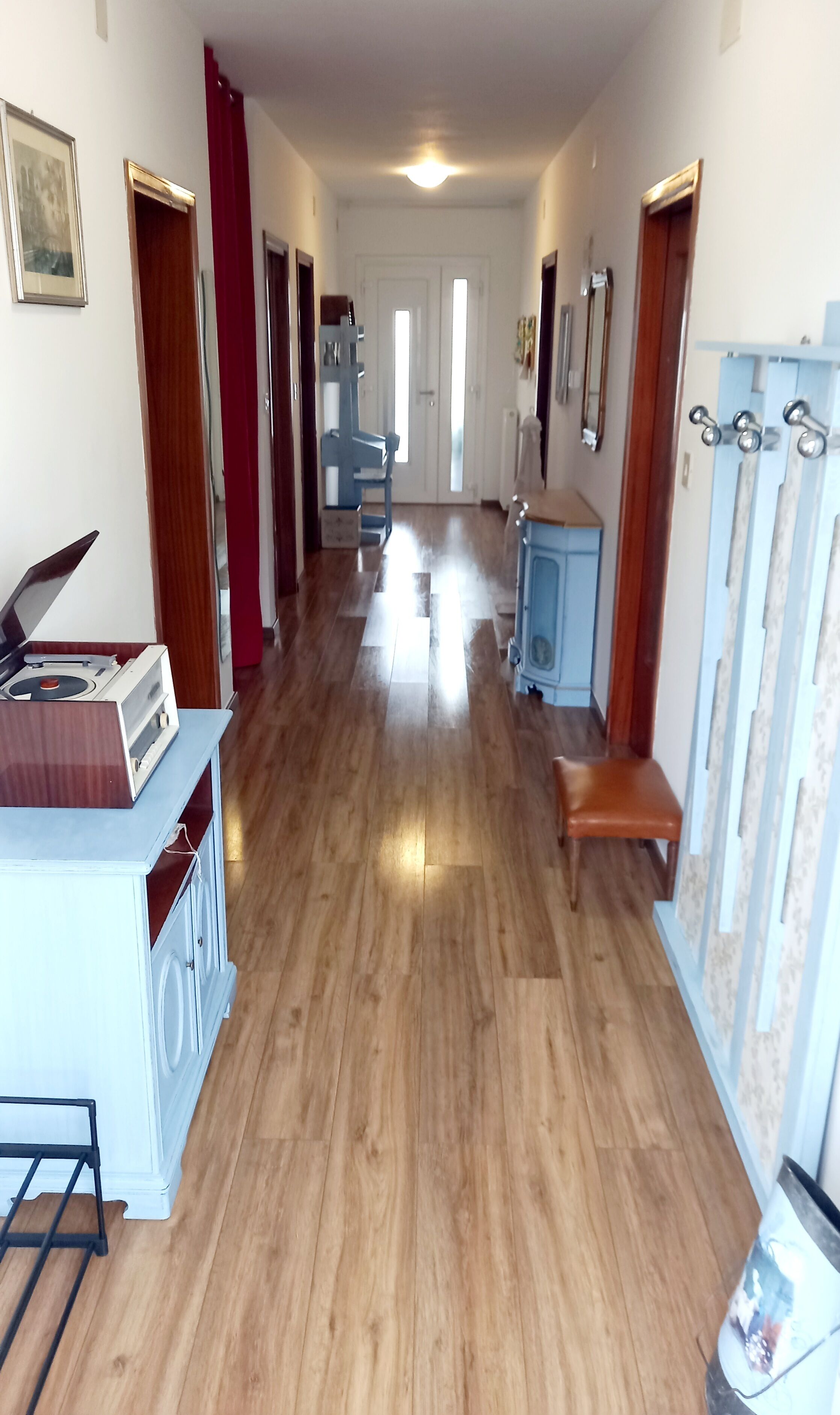A hallway with wooden flooring, a bench, a blue cabinet, and a white cabinet with a radio.