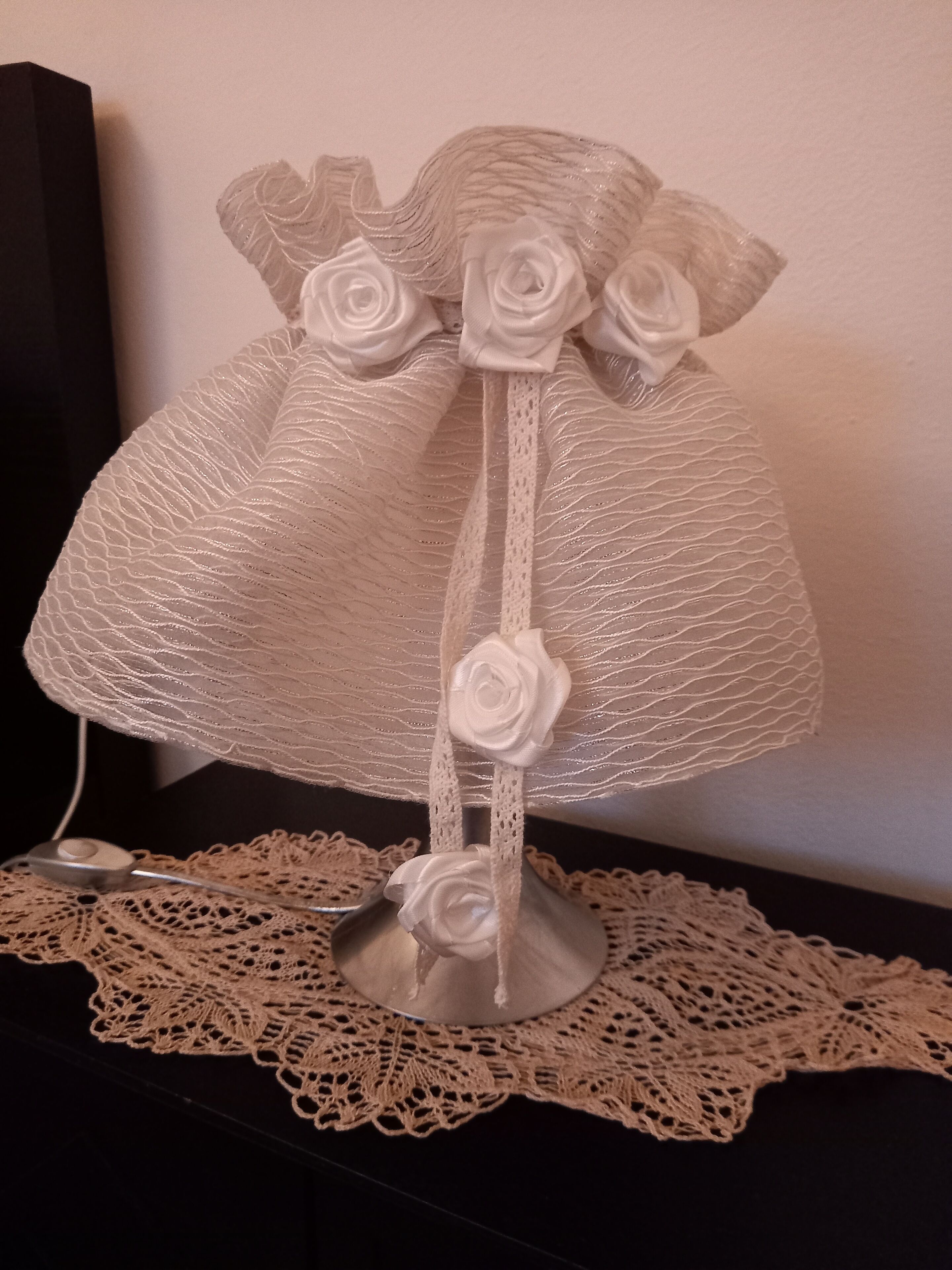 Un jarrón de cristal decorativo con base de encaje y tres rosas blancas sobre una mesa.