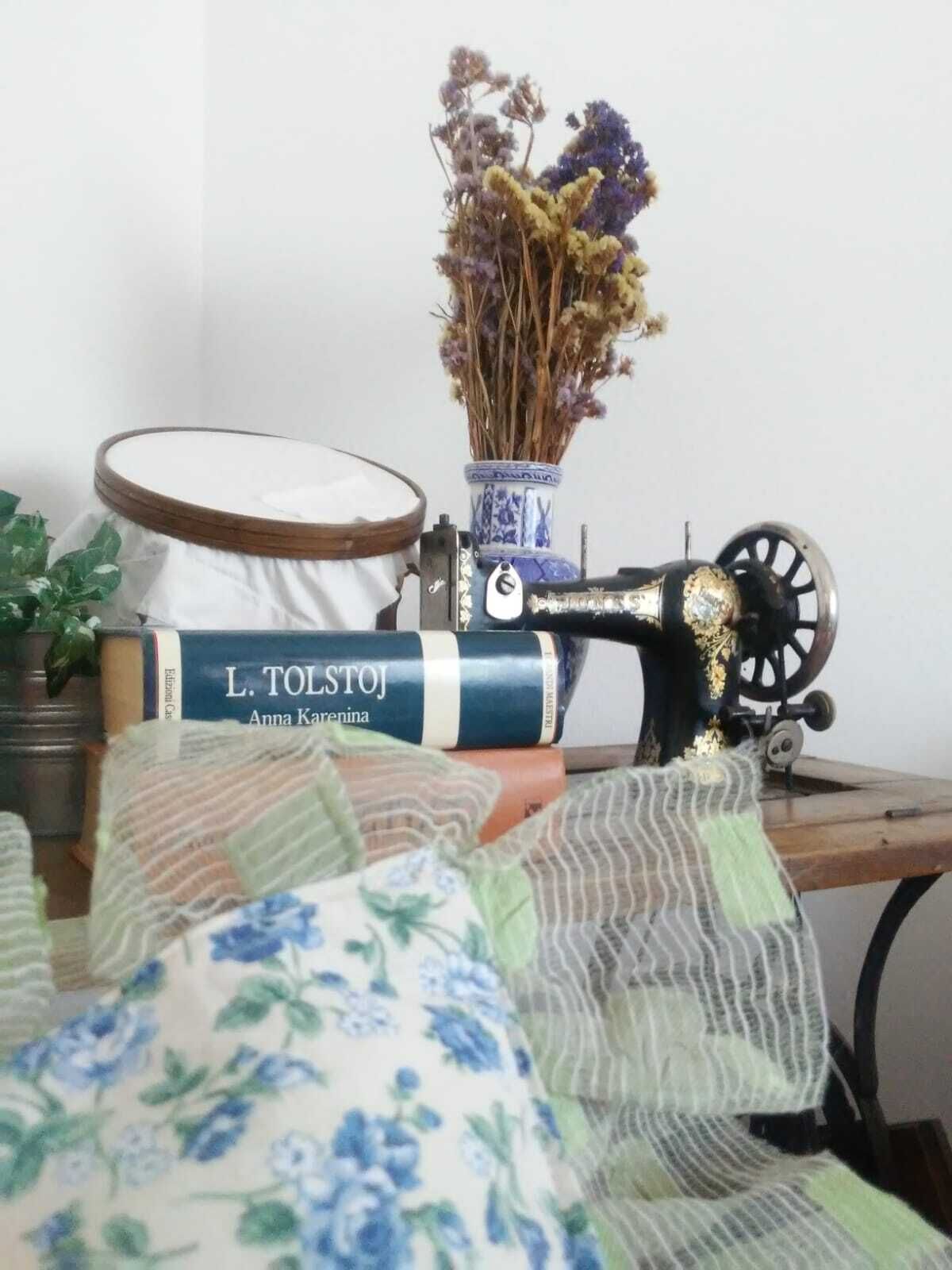 En gammal symaskin, en bok med titeln ”L. Tolstoj, Anna Karenina” och torkade blommor i en vas på ett träbord.