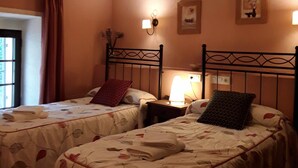 A room with two beds, each with a headboard and a bedside table with a lamp. There are two wall-mounted light fixtures and two framed pictures on the wall. - Casas Rurales Los Arrayanes for 4 people (Ronda)