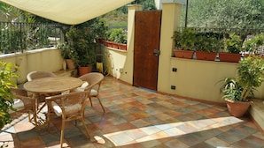 A patio with a round table and wicker chairs, surrounded by potted plants and a wooden door. - Apartment in villa with use Pool. Terrace, Parking (Agrigento)