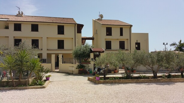 A residential building with multiple balconies, a gravel courtyard, and potted plants. - Apartment in villa with use Pool. Terrace, Parking (Agrigento)