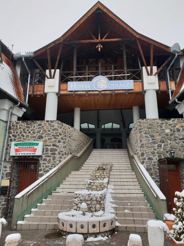 A hotel entrance with a stone facade, a wooden staircase, and a sign for a pizzeria.