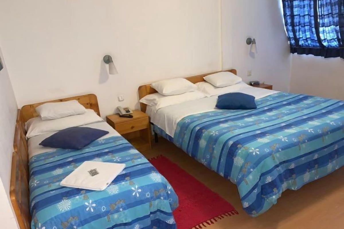 A room with two single beds, each with a wooden headboard, a bedside table, and a lamp.