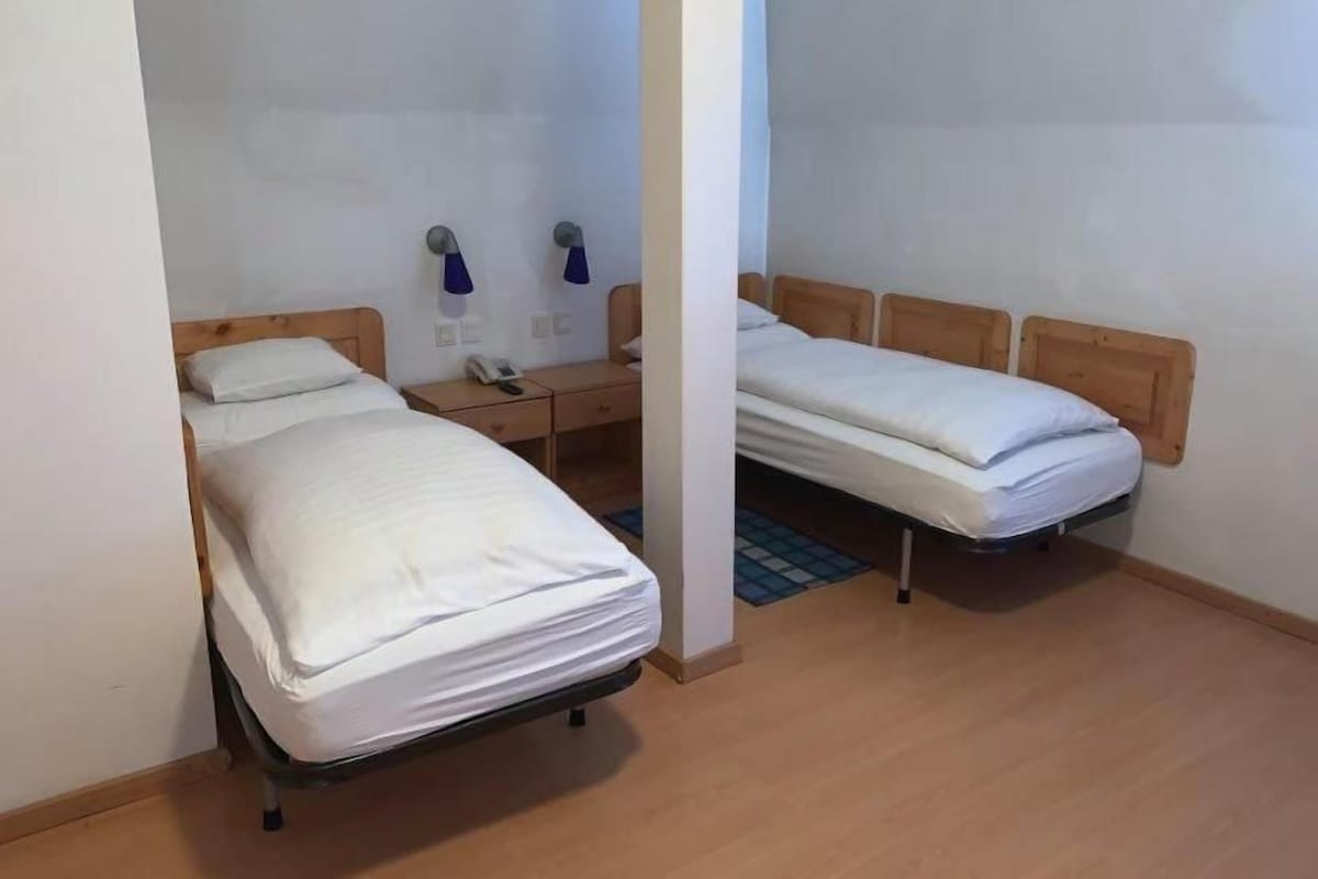 A room with two single beds, a wooden headboard, a bedside table with a lamp, and a telephone.