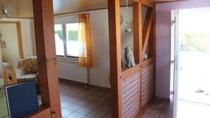 A room with a wooden ceiling, a brick wall, a window with curtains, and a door leading outside.