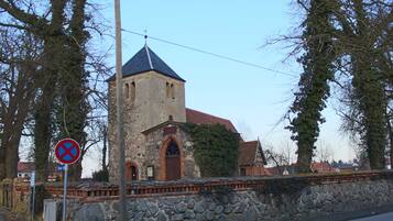 En historisk kyrka byggd av sten, med ett klocktorn, en stenmur och en skylt som förbjuder parkering.