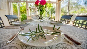 Mesa posta para refeição com prato, garfo, faca e copo, e um vaso com flores.
