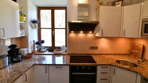 Una cocina moderna con armarios blancos, encimera de granito, horno integrado y pileta de acero inoxidable.