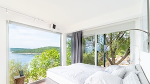 Un dormitorio con un ventanal grande que ofrece vistas panorámicas de un cuerpo de agua y vegetación.