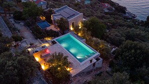 An aerial view of a property with a swimming pool, stone architecture, and surrounding vegetation.