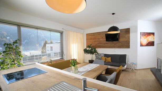Eine moderne Küche mit einer zentralen Kochinsel, einem Essbereich mit einer Sitzecke und einem an einer Holzwand befestigten Fernseher.