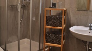 Ein Badezimmer mit einer gläsernen Dusche, einem hölzernen Ablagefach mit gemusterten Kissen und einem Waschbecken mit Spiegel darüber.