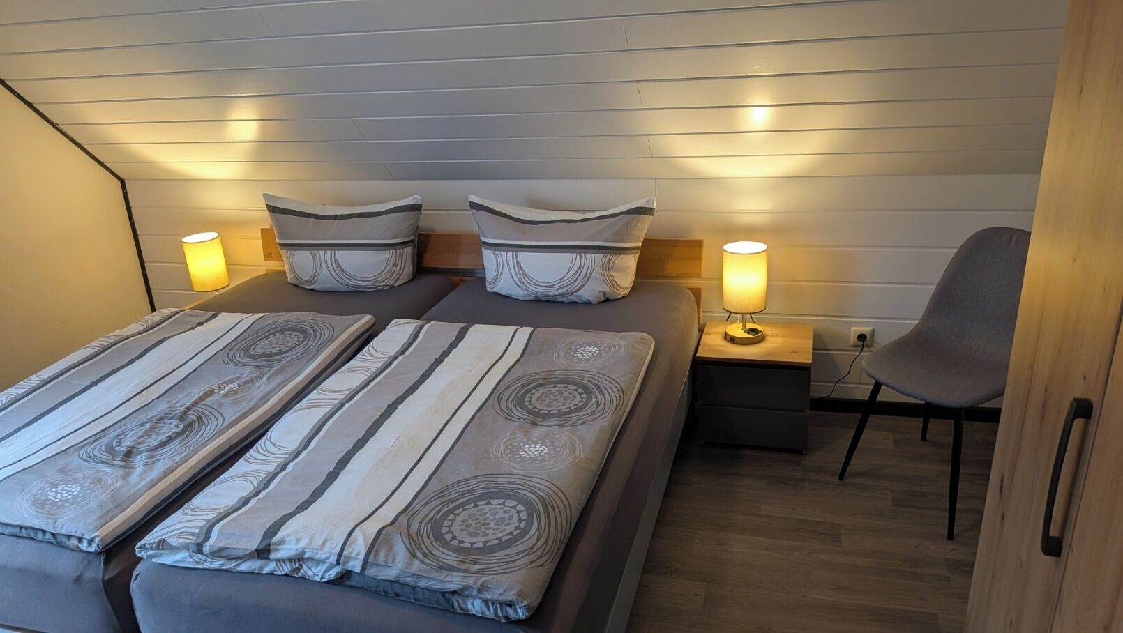 A bedroom with two beds, a chair, bedside tables, and lamps.