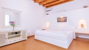 Een slaapkamer met een houten plafond, een bed met witte lakens, een kaptafel met spiegel en een klein bureau met lades.