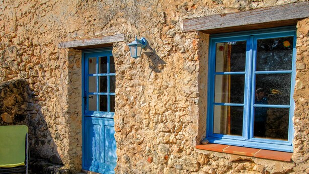 A stone building with a blue door and window, a small outdoor seating area, and a metal chair. - La Farigoule for 6 persons rental with shared pool nature and calm (Flayosc)