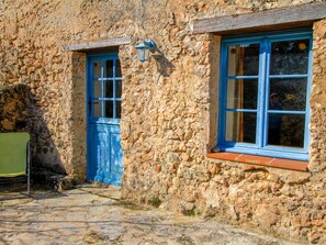 A stone building with a blue door and window, a small outdoor seating area, and a metal chair. - La Farigoule for 6 persons rental with shared pool nature and calm (Flayosc)