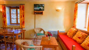 A cozy living room with a wooden sofa, a dining table, wicker chairs, and a TV mounted on the wall. - La Farigoule for 6 persons rental with shared pool nature and calm (Flayosc)