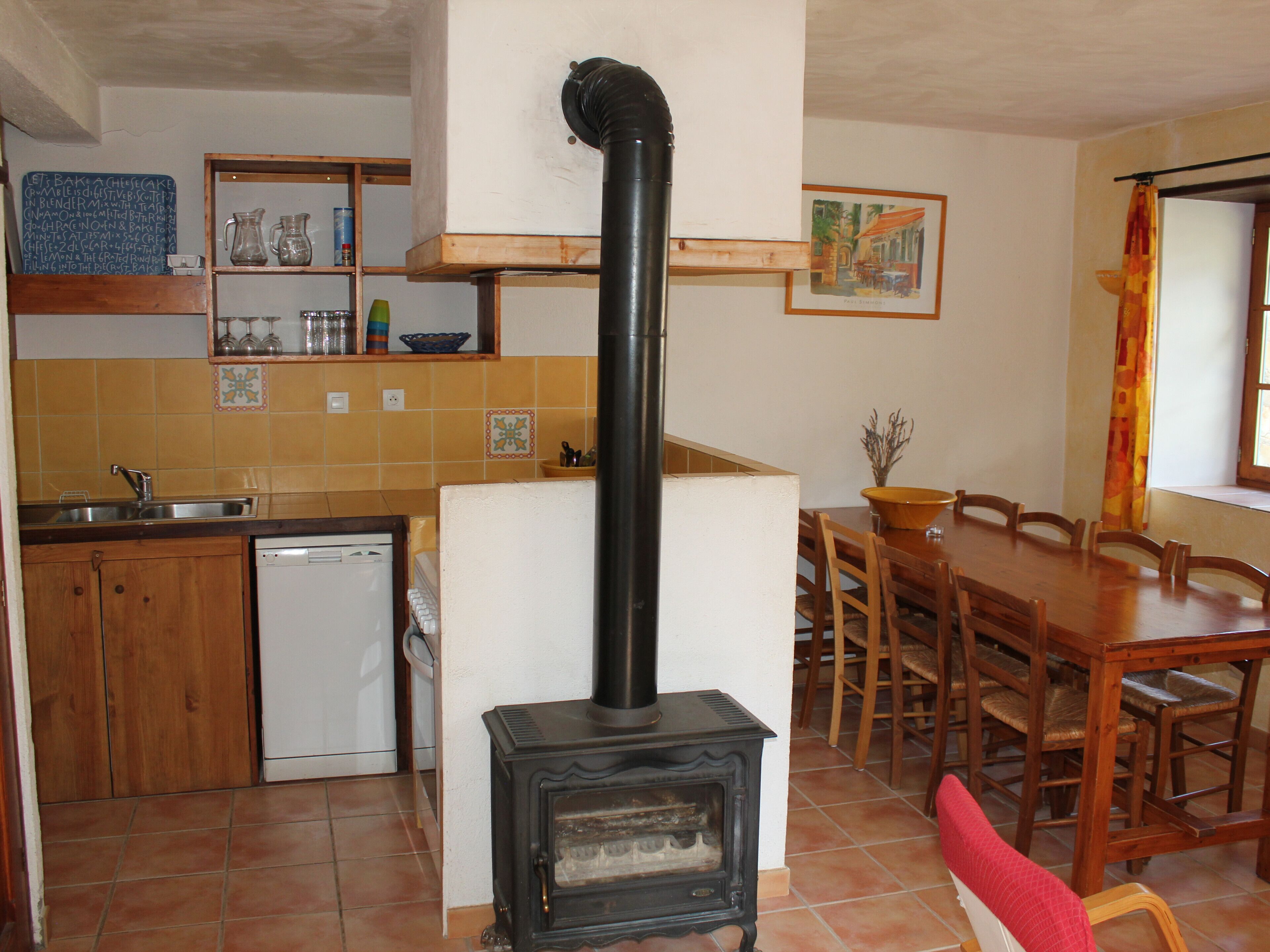 A kitchen with a wood stove, a dishwasher, and a dining area with a table and chairs.