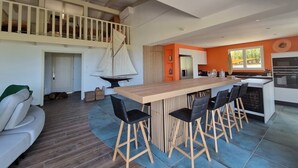 A spacious kitchen with a central island, a dining area with bar stools, and a loft bedroom with a balcony. - ALZONE_6-bedroom villa with a swimming pool and sea views in a quiet location (Porticcio)