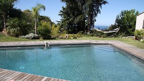 A rectangular swimming pool with a wooden deck edge, surrounded by lush greenery and a hammock. - ALZONE_6-bedroom villa with a swimming pool and sea views in a quiet location (Porticcio)