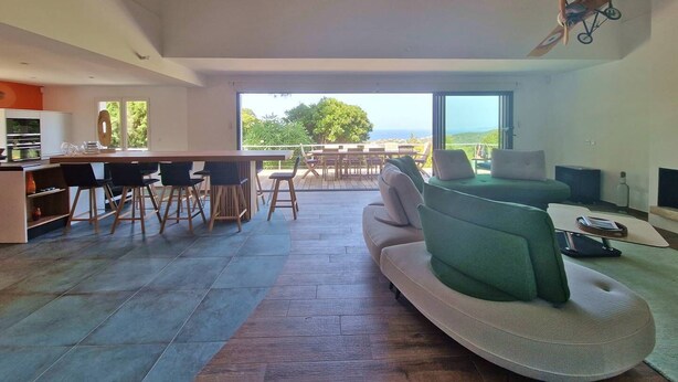 A spacious living area with a large sofa, dining table, and chairs. There is a view of the outdoors through large windows. - ALZONE_6-bedroom villa with a swimming pool and sea views in a quiet location (Porticcio)